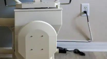 Close-up of a white exercise machine next to a wall outlet, with a black power cord plugged in and resting on a light wood floor.