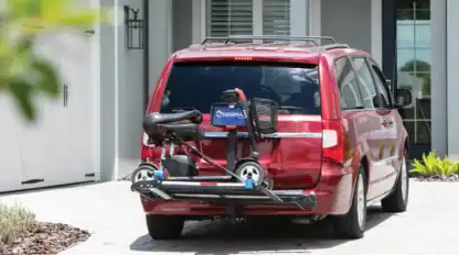 A red minivan parked in a driveway with a mobility scooter mounted on a rear lift carrier behind it.
