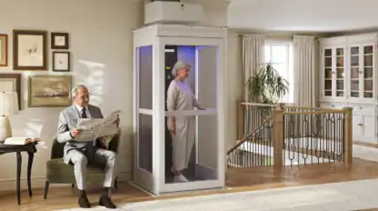 An older woman stands inside a home elevator, while an older man sits nearby reading a newspaper in a well-lit, modern living room with wooden floors and large windows.